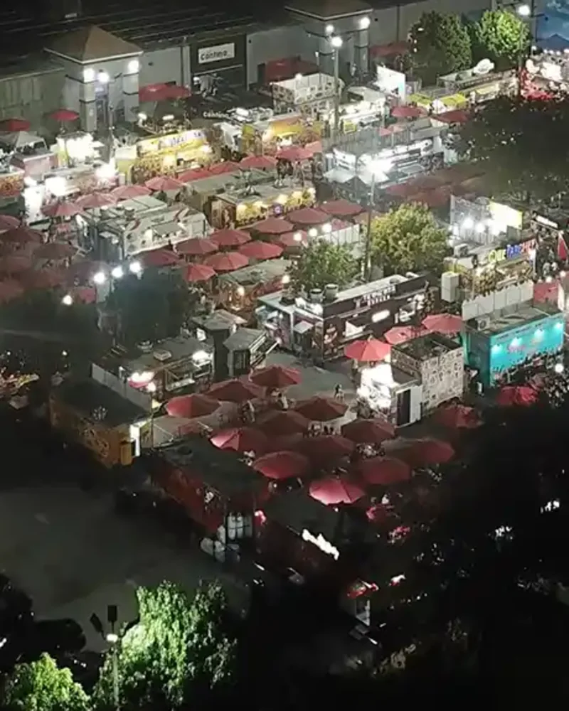 The World Food Trucks park after dark, rows of trucks and red canopies lit up.